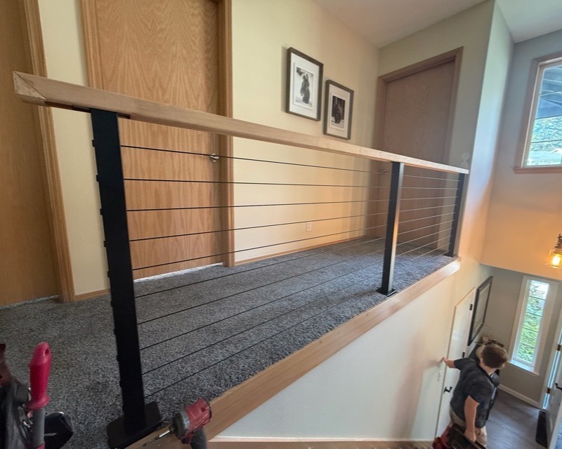 Trim carpentry — modern black cable stair railing with oak cap in Indianola